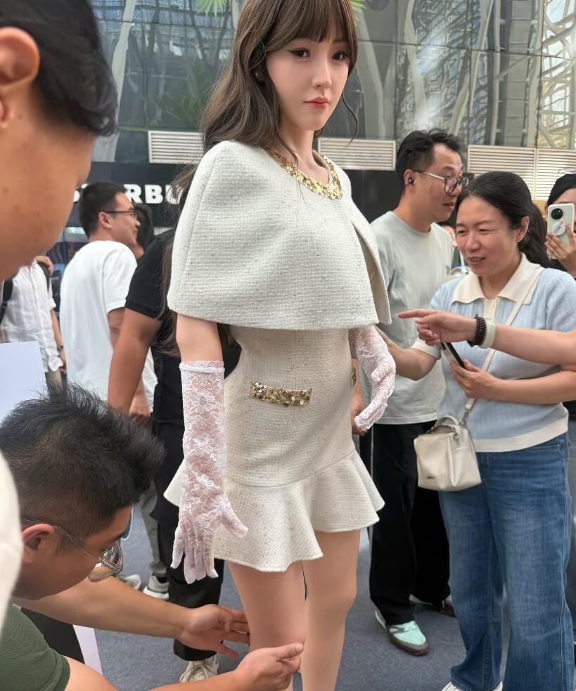 超市门口围观的真人感美女机器人，戳中了多少人对省心伴儿的幻想。今天路过超市门，一堆人围着看，我凑近才看清是个机器人，皮肤纹理、眉眼神态跟活人似的，重庆商场、长沙店里早有这种迎宾仿生机器人引围观，可真走近，它眨眼节奏、转身顿一下还是露了怯。咱老百姓过日子，算彩礼三金头大，吵起架整宿睡不着，看这机器啥都