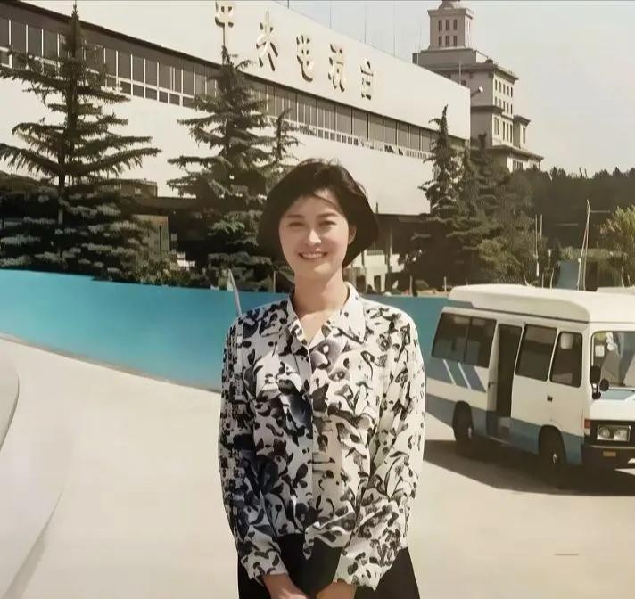 1994年春天39岁的敬一丹站在央视老楼前，碎花衬衫配着温和的笑，身后是墙上苍劲醒目的“中央电视台”几个大字和一辆老式采访面包车，那是她进央视的第六个年头。那一年《焦点访谈》开播，中国电视新闻走进千家万户最信任的岁月，她站在那个位置，赶上了好时候。如今再看这张照片，让人难受的不是她后来去了哪里，而是