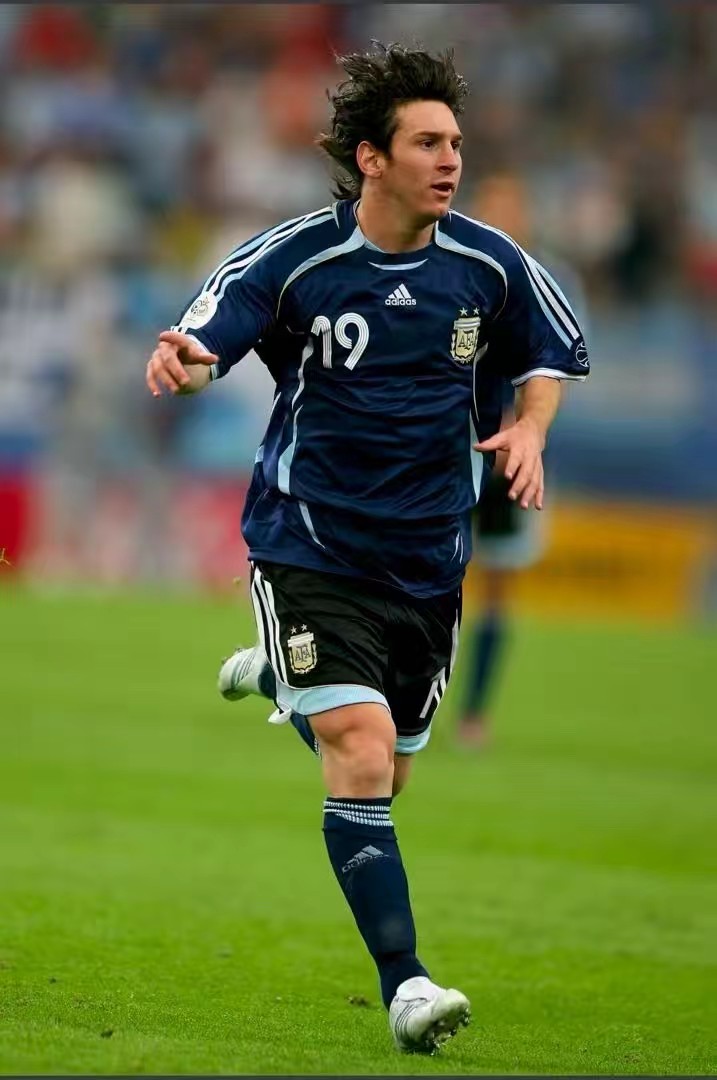 青涩少年，06世界杯19号梅西初登世界杯赛场
这张照片定格2006德国世界杯，年仅19岁的梅西身披阿根廷19号深蓝战袍，在绿茵奔跑。这是他第一届世界杯，青涩卷发，眼神充满冲劲。年少的他初登世界最高舞台，带着无限潜力登场。当年那个追风少年，自此开启传奇生涯，一步步成长为球