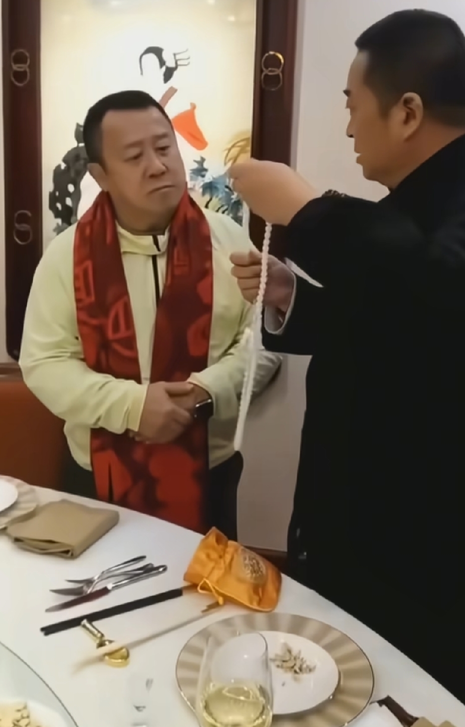 曾志伟与友人聚餐时，对方赠送他一串珍珠长手链，正在给他试戴。