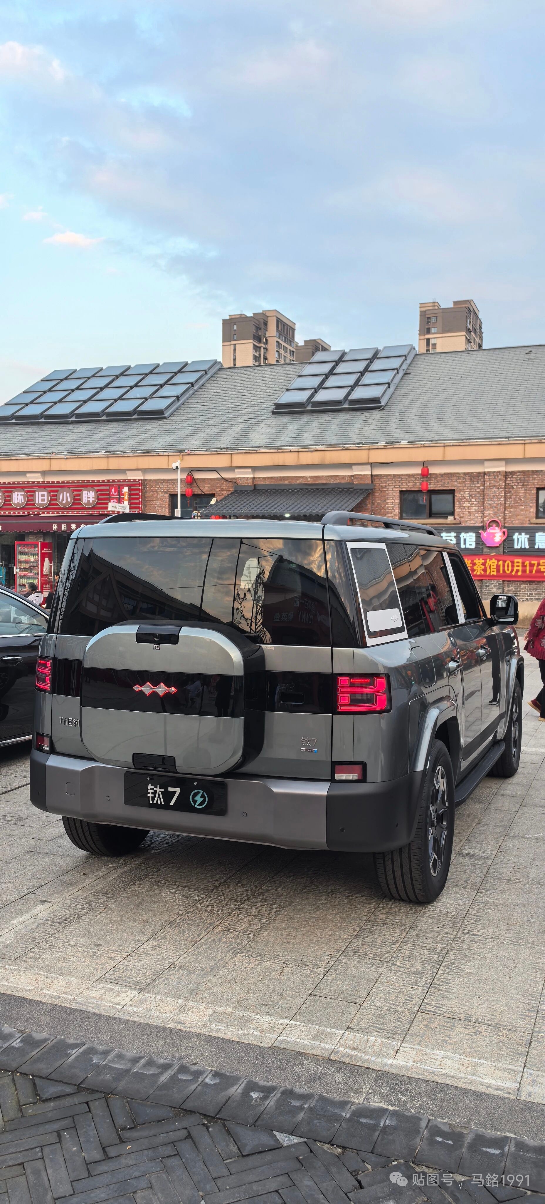 上周在商圈地下车库偶遇一台方程豹钛7，盯着看了快三分钟差点错过电梯。

方中带圆的车身线条完全没有硬派越野的笨重感，车长快5米却一点都不显得拖沓，轮拱外扩的肌肉感搭配隐藏式门把手，远看是气场两米的硬派狠角色，凑近了能摸到车身曲面的细腻过渡。

后来跟着它出车库走了两公里辅路，沿途至少有三个等红灯的车