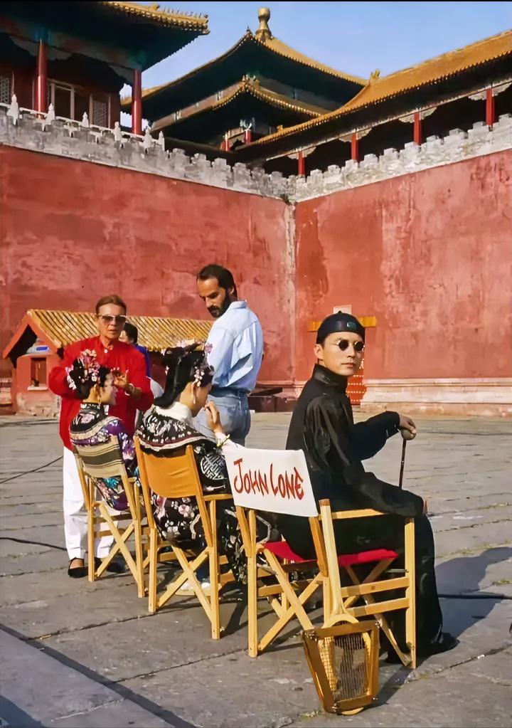 这张老照片太有年代感了！右边戴墨镜的正是尊龙，椅子上还写着“JOHN LONE”。

这部电影，最牛逼的地方绝对是取景，直接在故宫实拍！这事儿现在真是后无来者了。看这红墙黄瓦，剧组这排面当年没谁了。

不过话说回来，贝托鲁奇这种西方导演拍《末代皇帝》，确实带着点猎奇的眼光在看近代转型期的中国。但不管