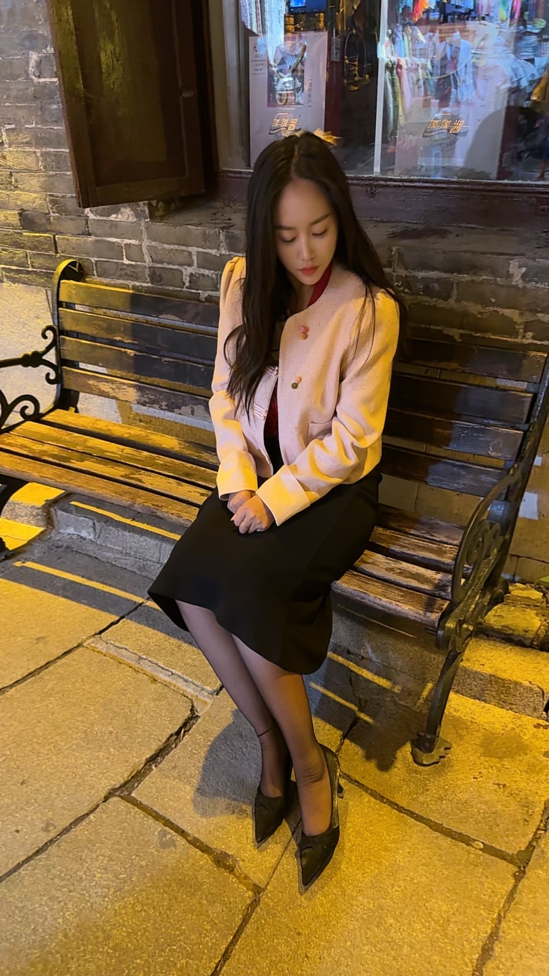 微微泛黄的灯光下，夜晚的街角，漂亮的小姐姐身穿粉色上衣，黑色短裙搭配黑...