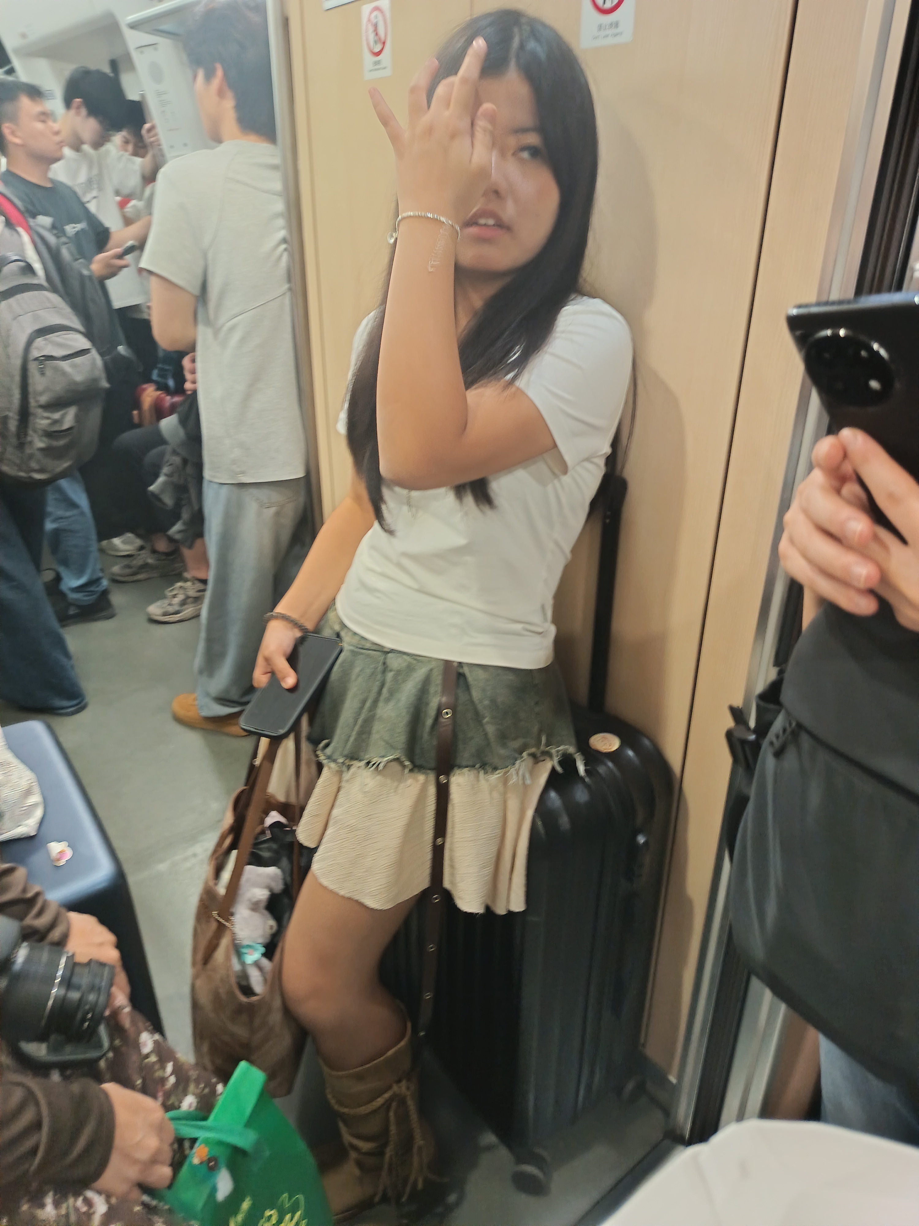 地铁上的时尚女孩，手拿手机，穿着牛仔短裙，背着大包，摆出酷酷的姿势。