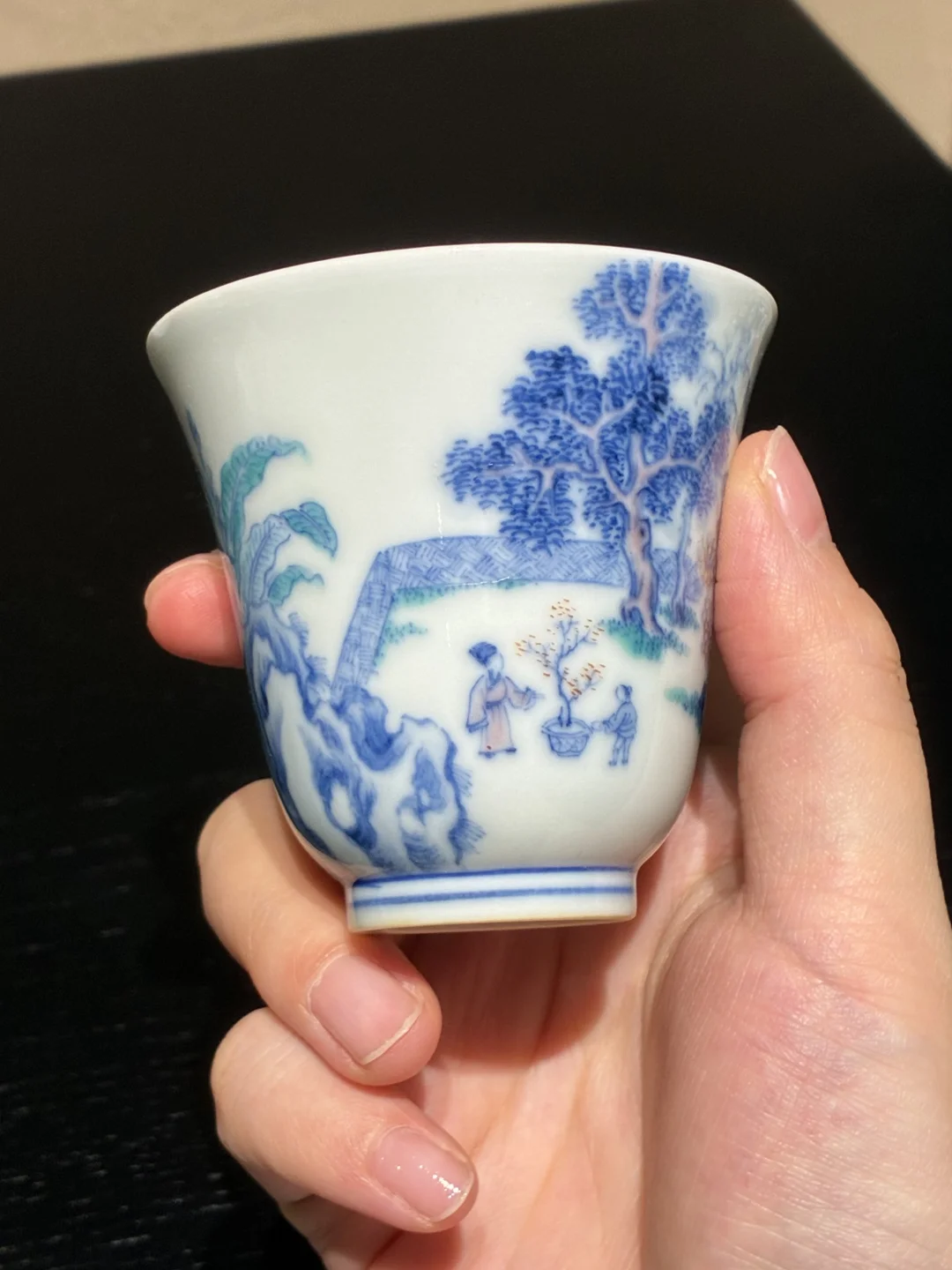 以青花勾勒庭院山水全貌，釉上填绘青绿芭蕉、苍劲古松、玲珑湖石，庭院屋舍错落其间；
