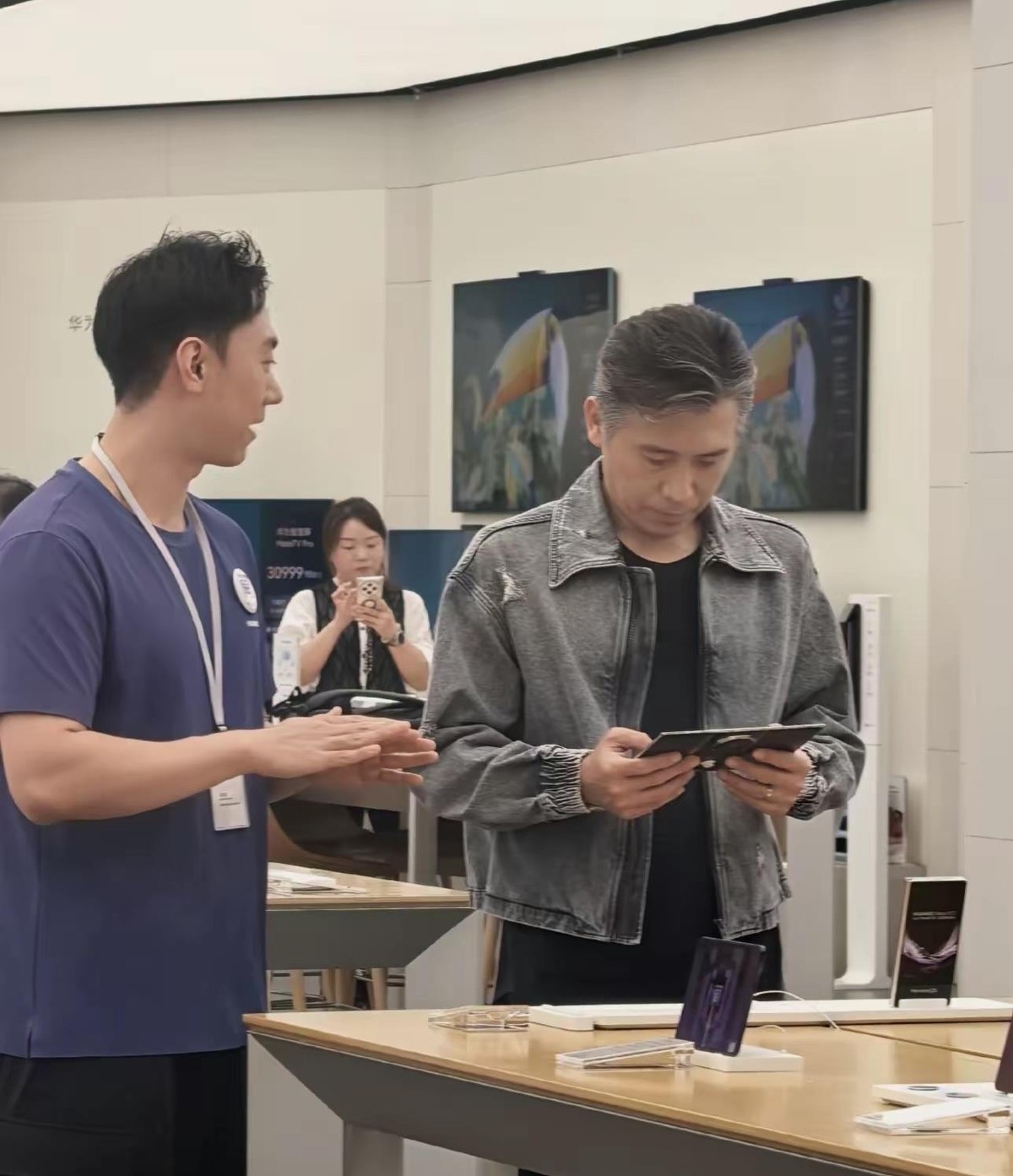 52岁的李乃文在重庆来福士华为门店试三折叠手机被路人拍到了，店员拿余承东那套物理防窥的梗给他讲解，左边折一下右边折一下，把他逗得直笑。画面里他穿得挺随意，人瘦高瘦高的，站在导购旁边一点不显年纪，就是头顶那片白发实在扎眼。有人翻出他之前跟胡军聊头发的视频，胡军说自己四十多白了是染的，李乃文接了一句自己