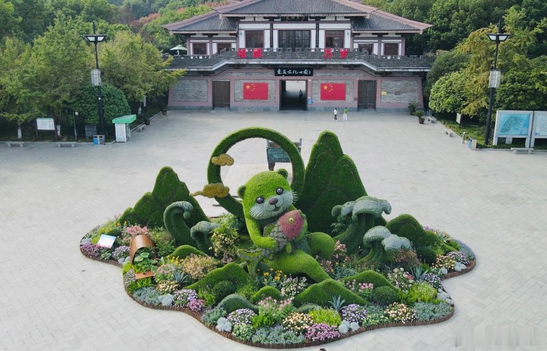 【富春碧韵，灵物伴江迎国庆】由富阳城管打造的《富春碧韵》立体花坛，以富春山水、水獭为意象，塑造水獭怀抱锦鲤的灵动造型，辅以波浪、群山、祥云，绘就生态图景。花坛融合立体绿雕与地面花境，运用多种观赏植物，层次丰富、色彩绚丽。作品彰显五水共治生态成果，传递绿水青山理念，献礼祖国华诞。*Q ​