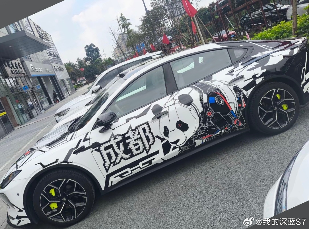 今天去店里静态摸了摸深蓝L06，实车就挺有得聊。展厅这台香芋紫确实拿捏人，溜背线条配上可升降尾翼，车尾看过去运动感很足。车头大灯边上的智驾小蓝灯特别吸睛，点亮后辨识度极高。门外那台“成都熊猫”机甲车衣更是视觉暴击，黑白拼色加上熊猫头和成都字样，瞬间换个气质。L06这“百变皮肤”的玩法， ​
