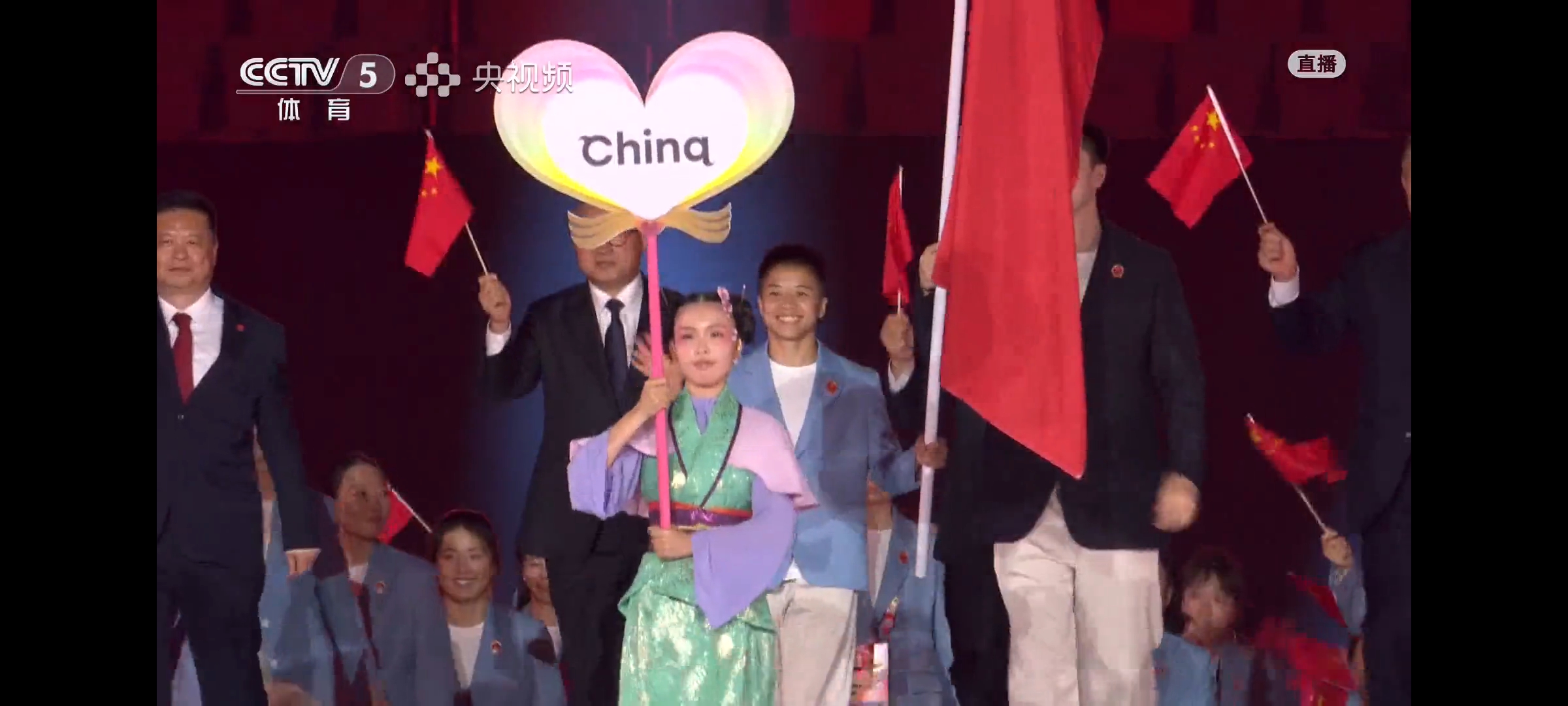 名古屋亚运会开幕式上，中国队入场，乒乓球项目的代表是领队王励勤，其他人没参加入场式，个子高，显眼，带着微笑，拿着小红旗🚩观赛席的丁宁和大家互相致意。女篮，刘禹彤，王思雨入镜。
