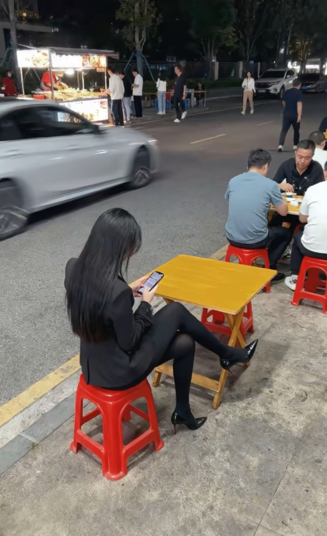 穿着时尚的小姐姐在热闹的夜市摊上等待就餐。