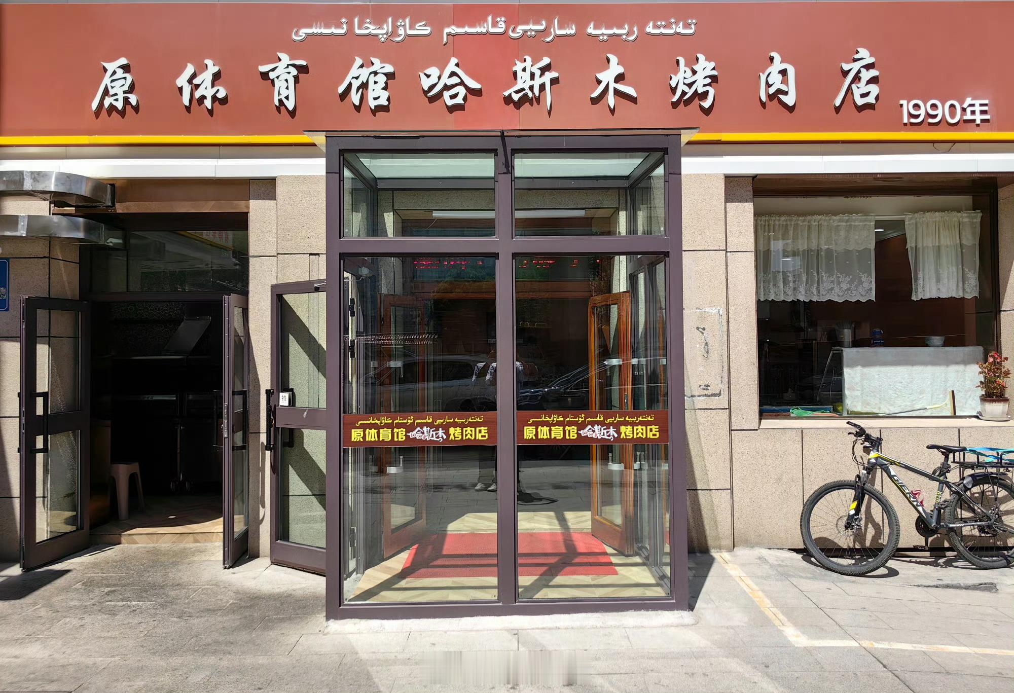 #乌鲁木齐[超话]##拍客老李拍天下##幸福生活e起拍##寻美新疆##三餐四季##我的美食日记# 1990年4月，哈斯木在南门体育馆大门西侧大树底下，开起了只有两张桌三条凳的烤肉摊，因价格低味道好趋之者众，印象中女儿才几岁常跟着我们去排队占座，那棵被油烟熏黑的树、熏黑的电风扇、端肉维吾尔小女孩（当年 ​