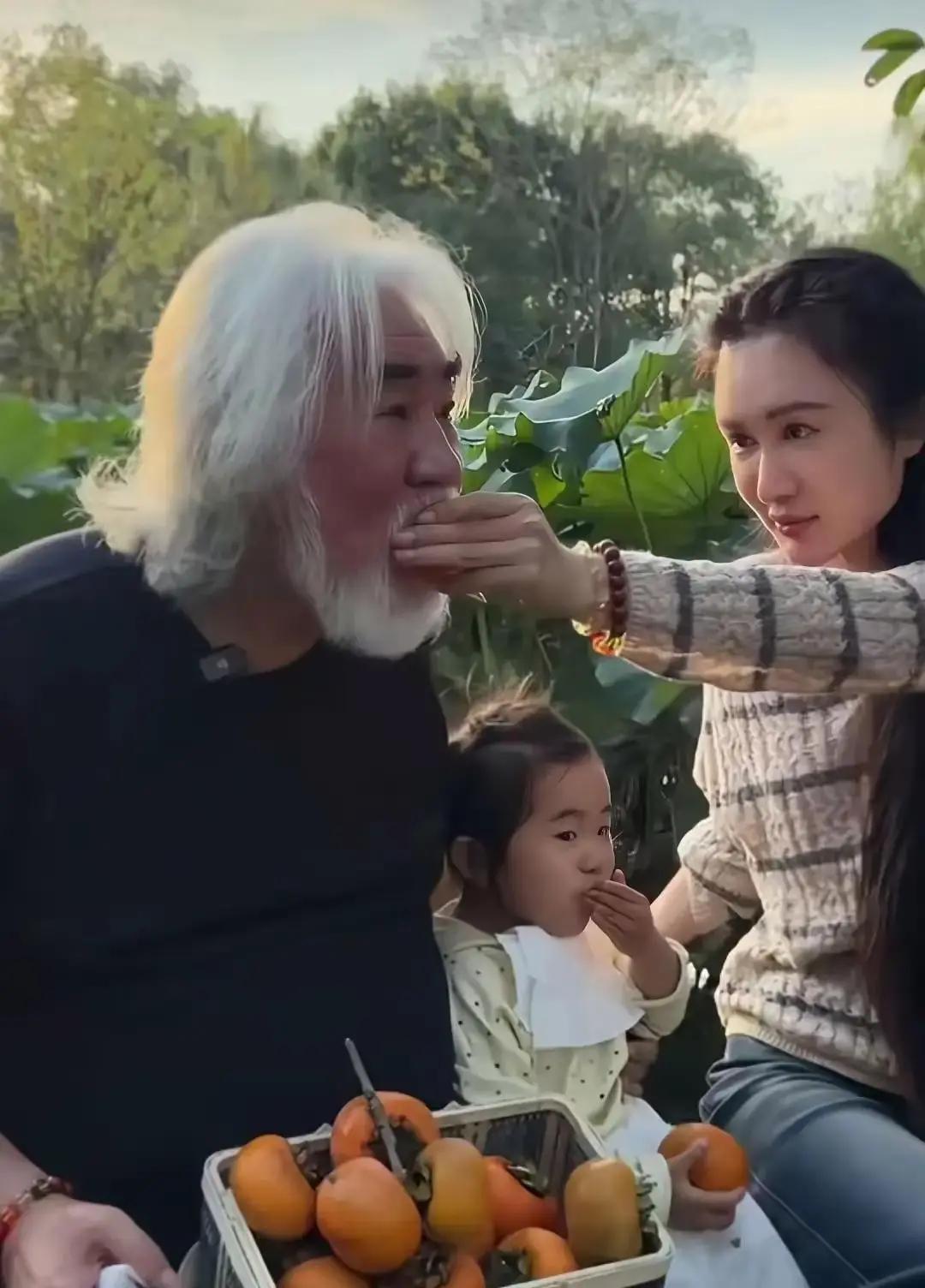 七十多岁还能把两岁多的闺女稳稳抱起来举高高，张纪中这身子骨确实让人不服不行。
网上但凡提到他们家，评论区总免不了有些冷嘲热讽，可人家两口子压根不当回事，照样慢悠悠过着自己的小日子。
这不，趁着秋天柿子红透，一家人跑去果园摘果子。
两岁的小女儿看中树梢上的大甜柿，够不着急得直蹬腿。张纪中当爹的二