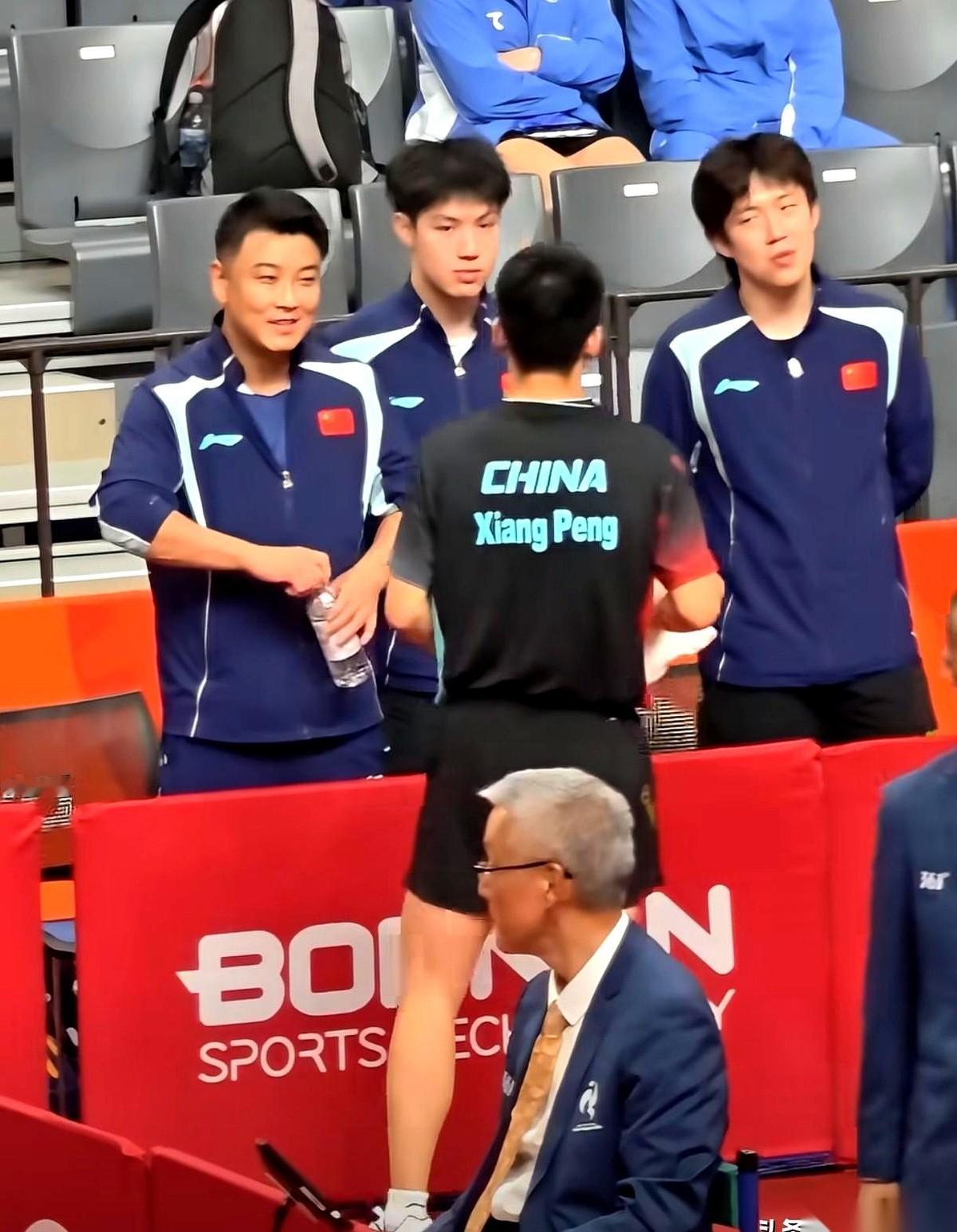 2026爱知·名古屋亚运会乒乓球男团小组赛，局间休息时向鹏走下场，教练王皓迎上去递水布置战术。
旁边的王楚钦安静等着，直到教练说完，他才凑近去低声分享对抗的细节经验。
刚刚回合暴露出的问题，正等着接收完指示的人重新回到赛场去解决。
你看这一幕，其实就是个特别真实的团队缩影。
大家仔细琢磨一下这短短一