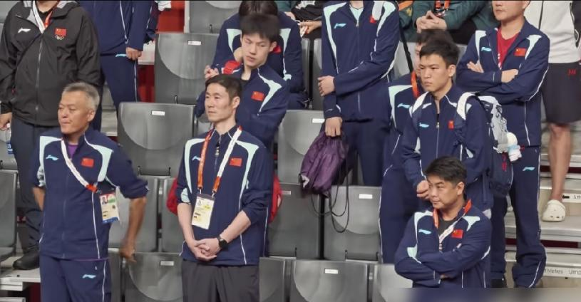 赢了都不敢笑，这金牌拿得比输了还憋屈！
名古屋亚运会乒乓球男单决赛，林诗栋4比0横扫王楚钦拿下金牌，整场比赛只用了32分钟。但真正让全网炸锅的不是比分，是赛后镜头扫到教练席的那一幕——总教练秦志戬下意识抬起手想鼓掌，手都举到胸口了，余光一扫周围，硬生生缩了回去，顺势摸了下鼻子掩饰尴尬。旁边王励勤、王