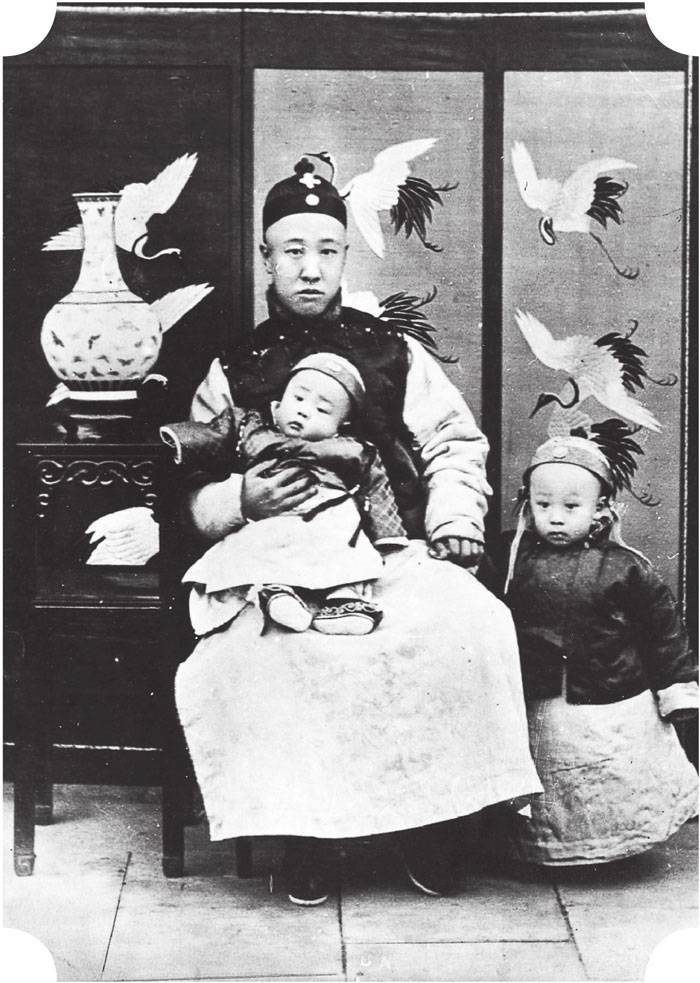 拍摄时间：约1906年
地点：北京醇亲王府
末代皇帝溥仪，时年三岁，立在父亲载沣身旁，此时溥仪即将被选中入继大统，成为宣统皇帝；父亲载沣也即将成为大清监国摄政王，载沣怀中抱着的是溥杰。