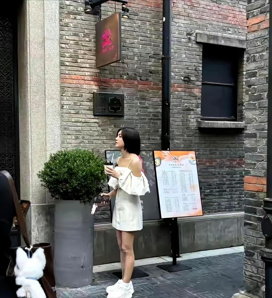 陈妍希上海被偶遇，白裙厚底鞋，真人瘦小只，娃娃脸淡妆很显嫩。白露肩裙轻盈，厚底小白鞋却笨重，审美小翻车，但状态很减龄。