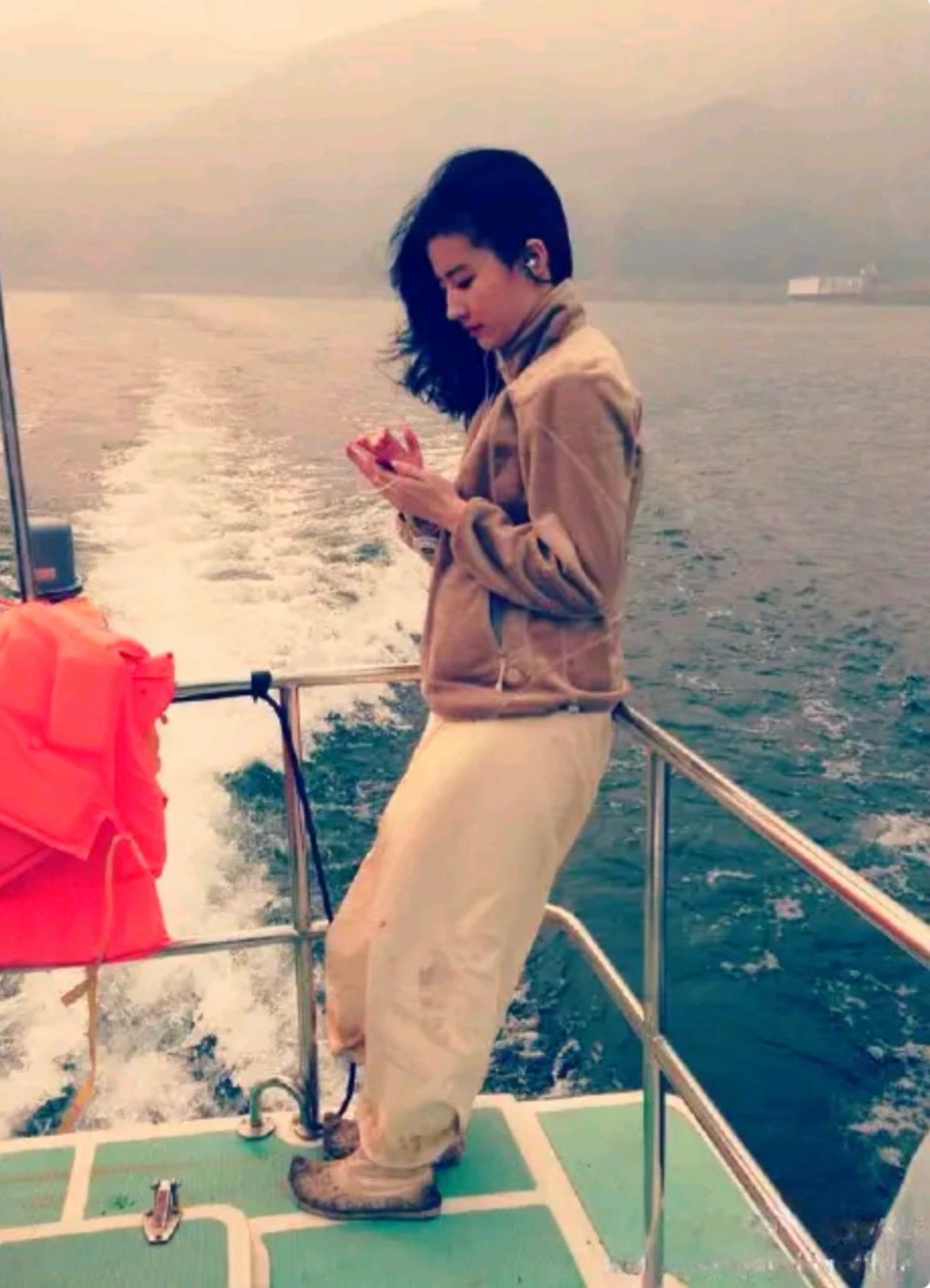 2013年，刘亦菲晒出她拍戏时，坐小快艇往返拍摄地的一张照片。

刘亦菲依靠在栏杆上，戴着耳机，听着歌，脚上和裤腿上都有泥。

这张照片，虽然不是很清晰，但当时26岁的刘亦菲，很有长发美少女的样子。刘亦菲