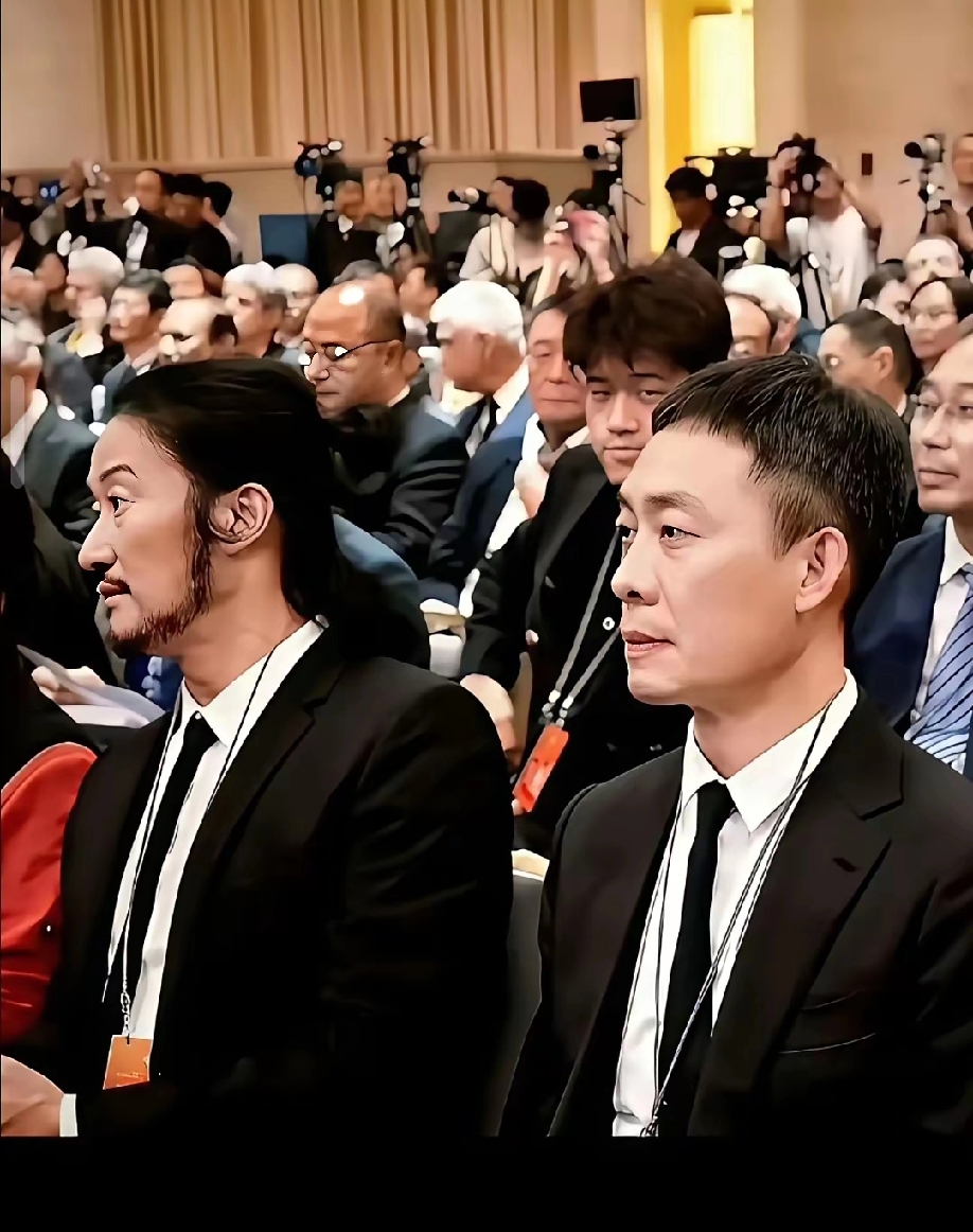 同框坐在会场，吴京和张译的反差感直接拉满。
 
52岁的吴京蓄起长发络腮胡，这身装扮看上去仿佛老了十岁，褪去往日荧幕利落硬汉形象，多了很重的沧桑感。
 
旁边48岁的张译，短发收拾得干净利落，神态沉稳内敛，整个人精神干练。
 
同样一身黑色正装，坐在一起气质对比格外强烈。
 
一个粗粝厚重，一个清爽
