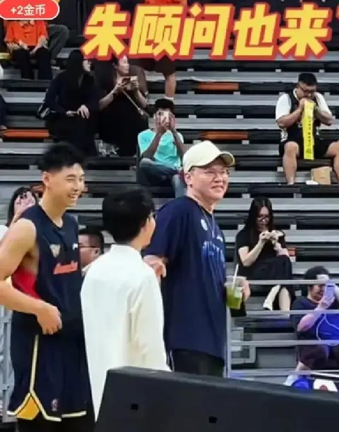 广东宏远主场打浙江稠州这场硬仗，看台上最抢镜的不是外援，而是朱芳雨手里那杯几块钱的蜜雪冰城。
堂堂宏远技术顾问，身板往那一坐本来就显眼，偏偏还戴了顶白色鸭舌帽想低调。结果手里的平民冷饮直接把接地气的画风拉满了。
坐在他旁边的是宏远少东家小陈总，俩人凑在一起聊得唾沫横飞、满脸堆笑。平时球迷天天在评