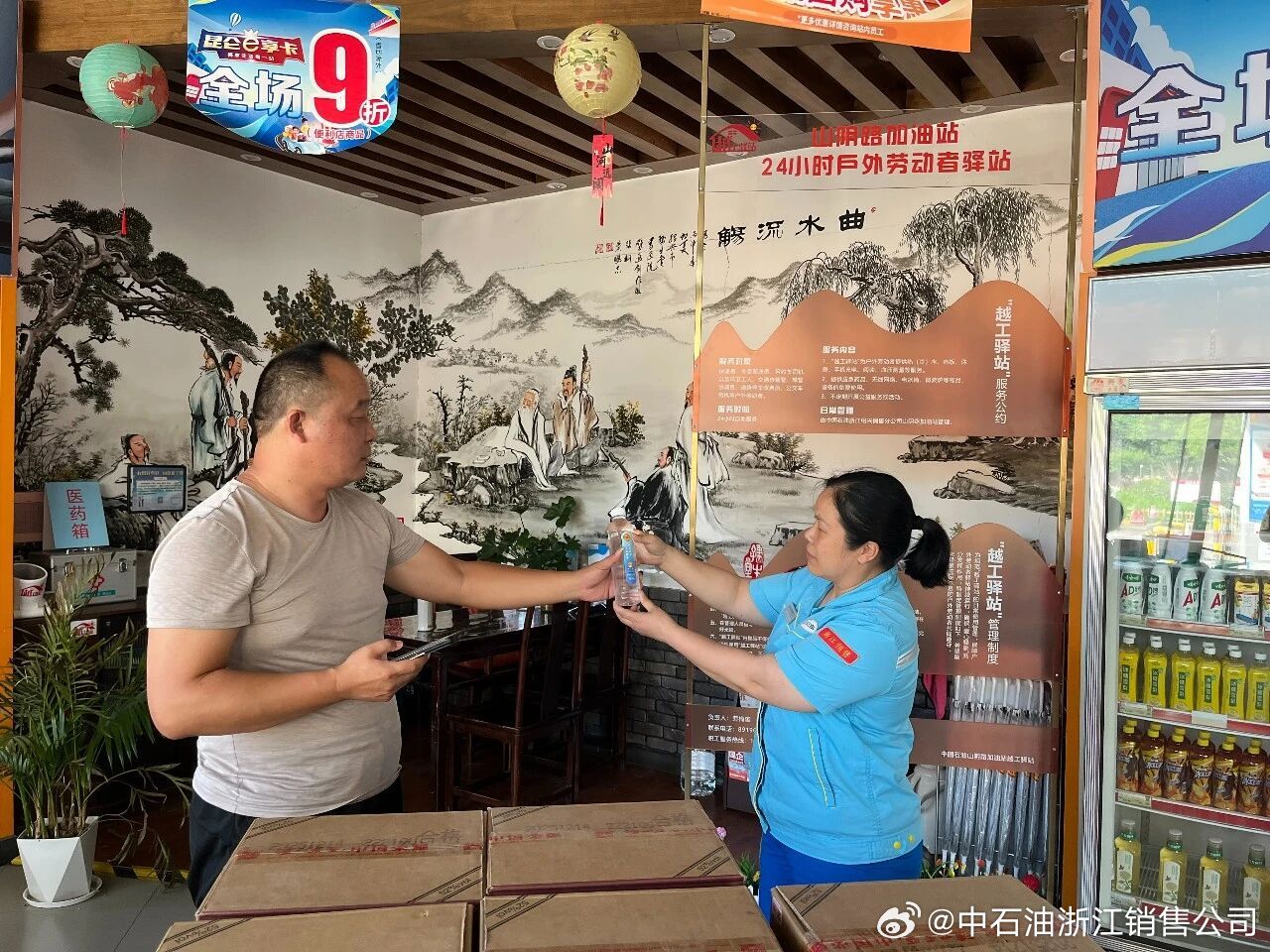 绍兴分公司山阴路加油站爱心驿站迎来前来避暑的环卫工人和货车司机。站内员工提前备好清凉矿泉水与冰镇西瓜，主动上前分发，贴心引导大家到空调休息区纳凉歇脚。驿站配备充电插座、座椅等便民设施，一位环卫工人趁着休息给手机充上电，由衷感慨户外作业无处落脚，在这里短暂休整、补给水电十分方便。大 ​