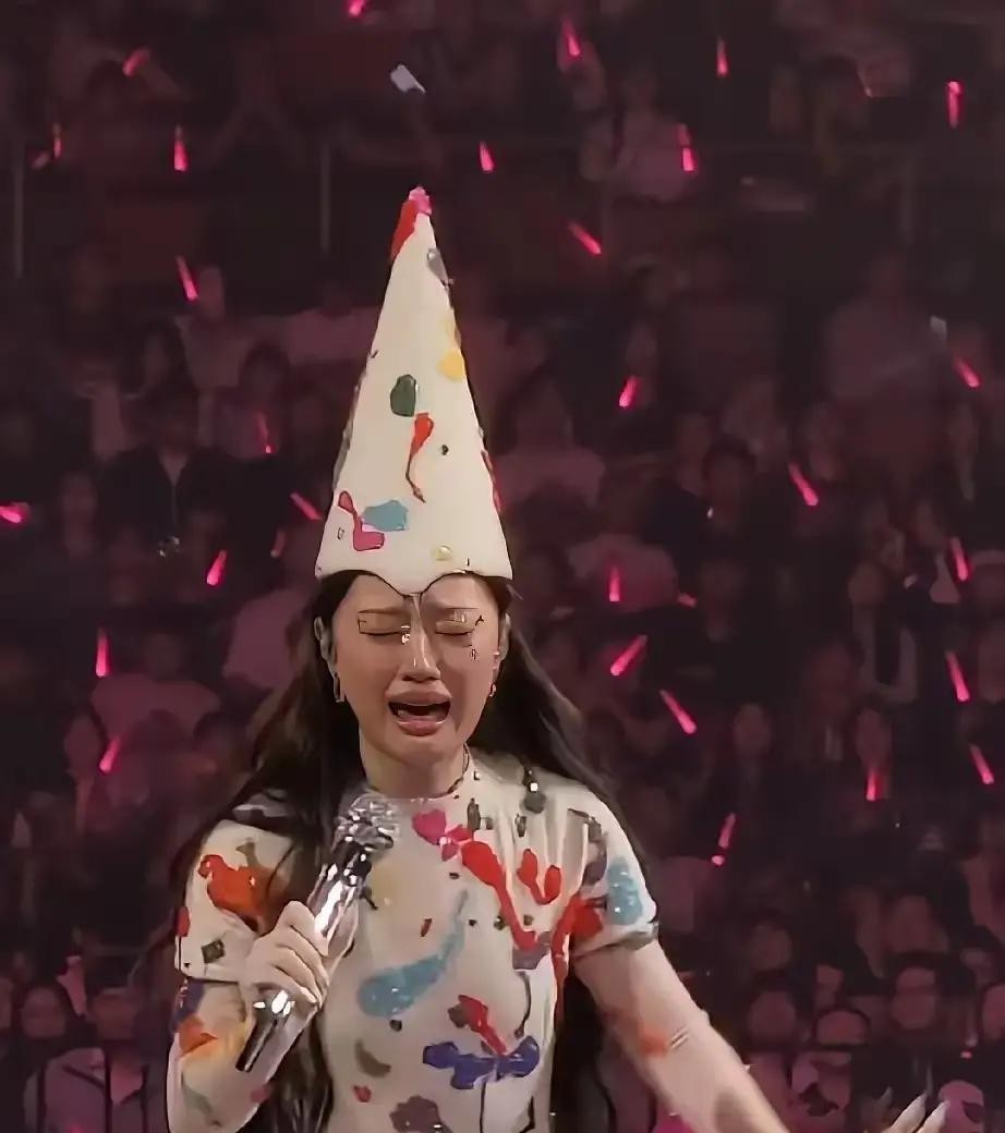 昨晚刷到几张演唱会现场图，差点以为谁家艺人得罪了团队在被公开处刑，定睛一看居然是新生代唱将单依纯

实在搞不懂她那个造型团队到底在玩什么先锋艺术

就拿成都那场演出来说，好好一个清冷气质的姑娘，脑袋上硬是顶着个莫名其妙的高耸尖顶帽

往下看更绝，身上罩着一件像是打翻了调色盘的花绿泼墨长裙

这套行头