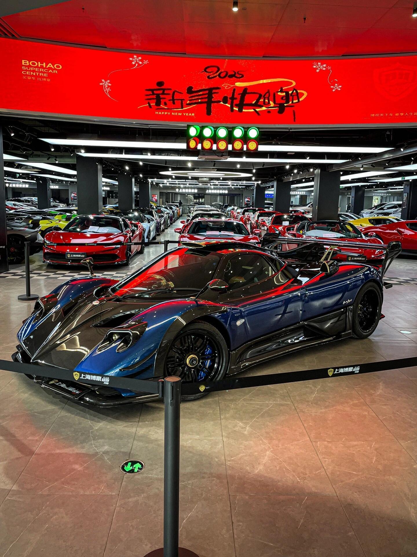 蓝碳帕加尼，贴地飞行，超跑展厅的绝对焦点
这蓝色碳纤维实车看着是真上头。全车大面积裸露的碳纹配上这种深邃的蓝，在展厅灯光下一打，质感直接拉爆。周围那一排排红色超跑全被抢了风头，在这台车面前活生生变成了背景墙。造型长得像外星飞船，巨大的尾翼加上贴地飞行的姿态，浑身上下散发着一种别惹我的野性。根本不需要