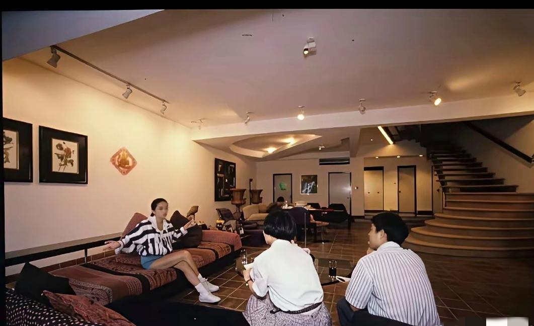 90年代，梅艳芳在香港豪宅客厅中，接受媒体专访时的一幕，室内空间宽敞开阔，弧形旋转楼梯、大幅装饰画，空间设计前卫，梅艳芳坐在沙发上，放松地和采访记者交流，神态自若。
​