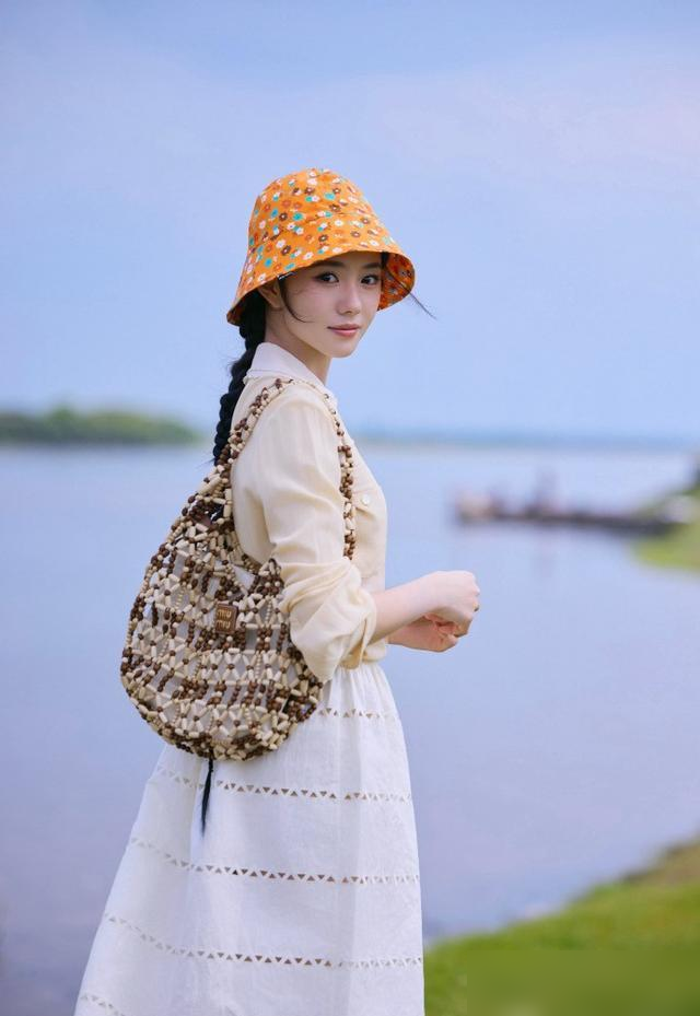 前脚还在红毯上撑着黑伞冷脸封神，后脚就蹲草堆里当牧羊女去了。
说的就是刘浩存。北影节那身黑色亮钻丝绒裙，雨里一站，全网喊黑天鹅。转头柏林全英文采访，气场直接拉满，哪还有半点刚出道时的怯生生。
结果六月这组写真一放，白裙子低马尾，往草垛子边一坐。不凹造型，不看镜头，全是自然抓拍。
一个拼了命往外