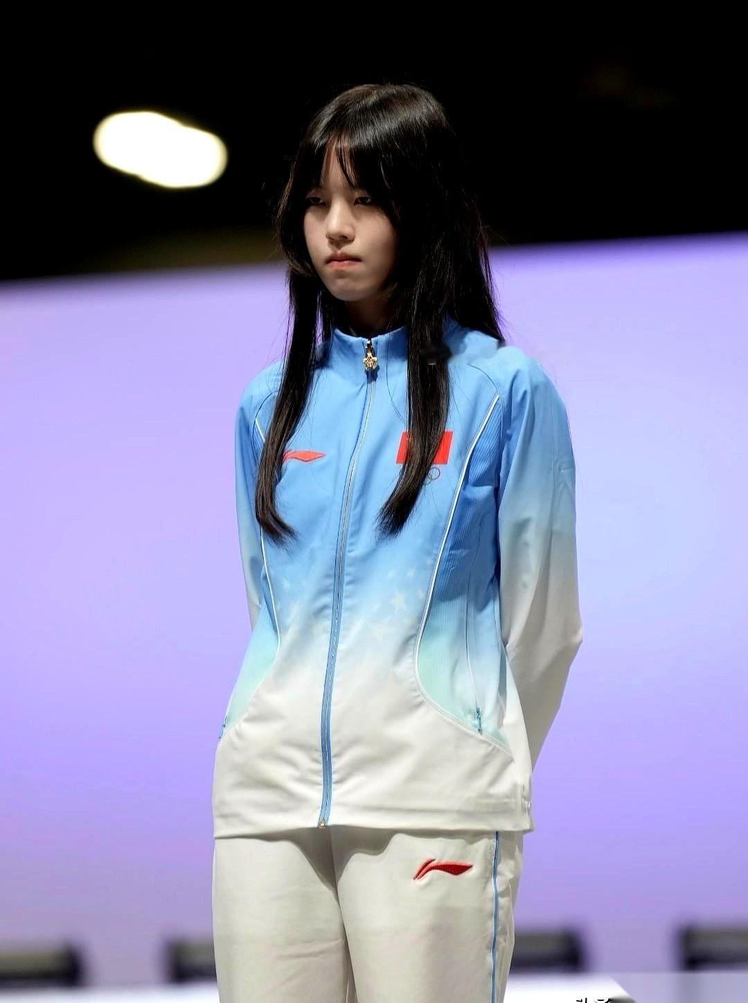 亚运会电竞项目的转播画面里，出现了一个极其“违和”的场景。
在一群穿着同款运动服、个头高大的男队员中间，夹着一个个头极其娇小的姑娘。
她叫穆欣月，游戏ID“桃晚安”，是这届亚运会上，全场唯一的女电竞选手。
目测身高连一米六都不到的她，站在队伍里，仿佛一个误入巨人阵营的高中生。但最抓人眼球的，不是她的