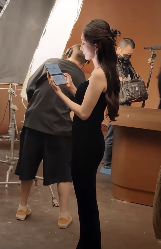 杨幂一张穿黑色抹胸裙的生图流出，直接把顶流女星的真实体态，扒了个底朝天。
镜头里，她拿着折叠屏手机拍广告。没了打光掩护，脖子前倾、含胸驼背的老毛病，彻底暴露。连骨盆前倾的僵硬感，都在紧身裙下无处遁形。
评论区吵翻了。有人拿她跟刘诗诗的天鹅颈死磕，叹息气质被体态拖垮。也有人翻出8月4日的机场旧照，