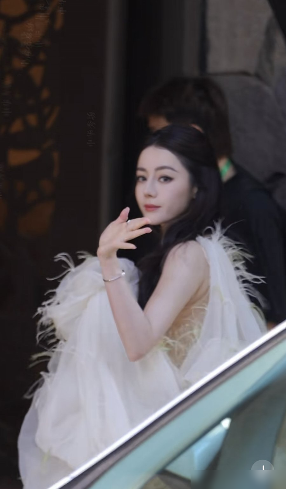 迪丽热巴广州这场生图，直接把内娱红毯和线下商演的差距撕开了。
10月19日阿道夫活动，她穿的是越南设计师Nguyen Phuc Tuan 2027春夏裸色透纱裙，绿钻点缀，单肩羽毛拖尾，配Mikimoto珠宝。不是高定，不是顶奢，但生图里那身段和脸，稳得离谱。
现场还发玫瑰花、脸颊比心、美萌连拍