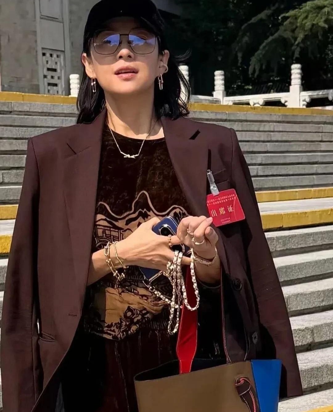 章子怡现身北京友谊宾馆，一顶黑棒球帽配咖啡色西装，硬是把“随便穿穿”穿成了高配版。

她耳朵、脖子、手腕一套蒂芙尼首饰齐上阵，手指上还叠着几枚戒指，旁边那只包一看就身价不低。外套看着像思琳那挂，整套搭下来，少说也是几十万的排面。

不过最有意思的是，章子怡私下这状态，比红毯上还松弛。脸部骨相太能扛镜