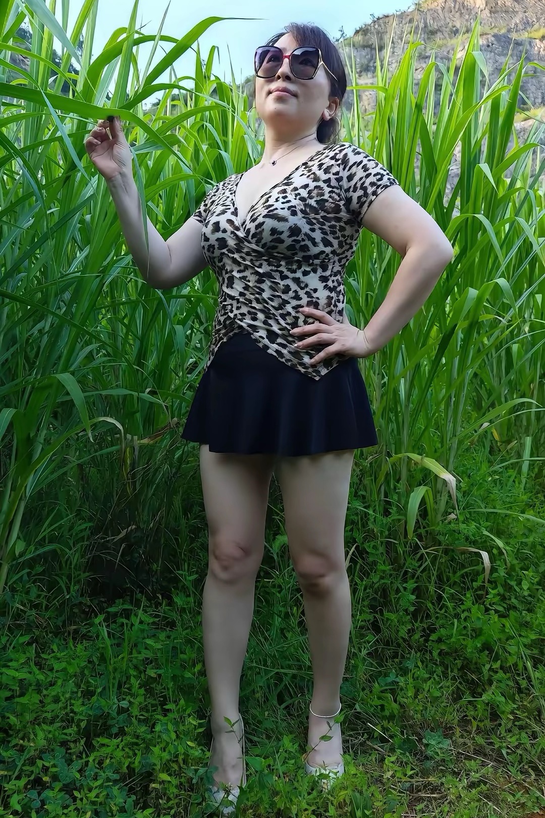 她身着豹纹上衣，在绿意盎然的户外，或立或摆造型或坐于石墙，姿态随性，与自然景色