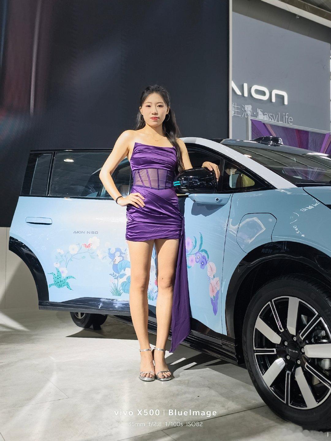 #vivo[超话]#灯光落于缎面，晕开浓郁的紫。
喧嚣的展厅里，自带一份张扬又从容的气质。
光影漫过肩头，把瞬间的姿态，妥帖收好。
不必刻意，自有风情。
紫色缎面裙子质感很出彩，和浅蓝色车身形成柔和撞色，灯光下人物轮廓干净，明艳又有气场。
#当你有了vivo##人像摄影##vivox500系列# ​